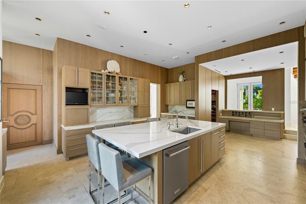 A modern kitchen features light wood cabinetry, a large marble island, and stone flooring — 3315 BAY SHORE ROAD, SARASOTA, FL