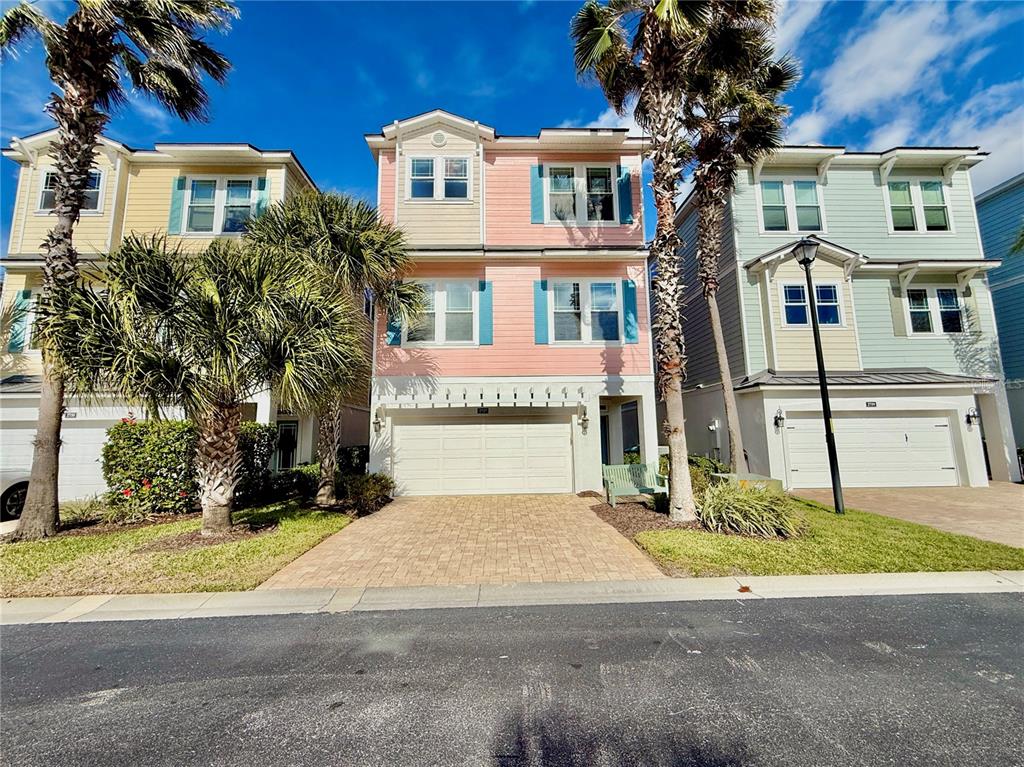 A three-story pink house with a two-car garage sits between two other residential homes — 2727 MORNING LIGHT COURT, FLAGLER BEACH, FL