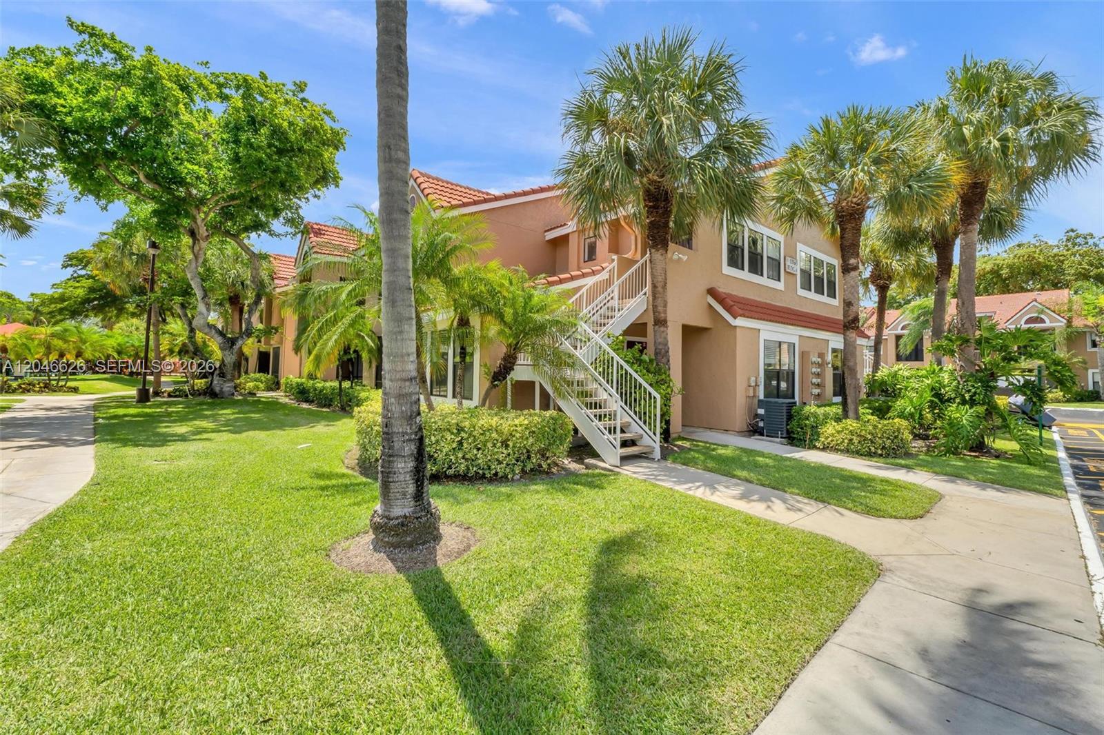 An exterior view of a two-story apartment building with a white staircase and palm trees — 15560 SW 104th Ter # 6112, Miami FL 33196, MIAMI, FL