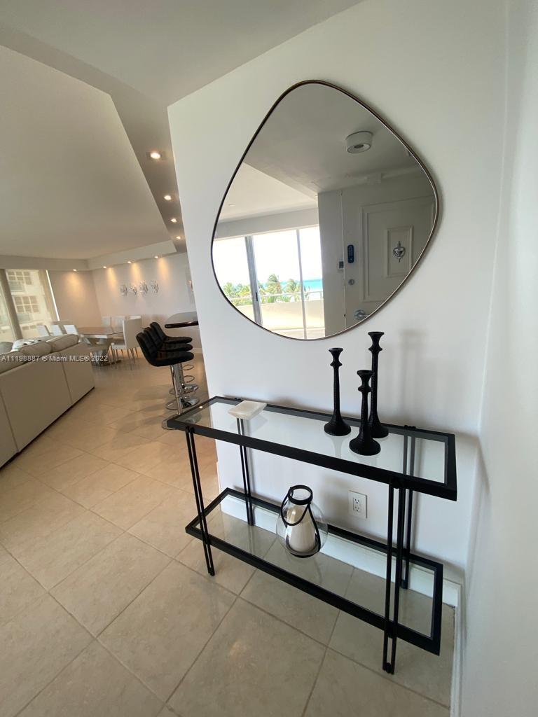 A modern entryway features a glass console table, black candlesticks, and an organic-shaped wall mirror — 5151 Collins Ave # 531, Miami Beach FL 33140, MIAMI BEACH, FL