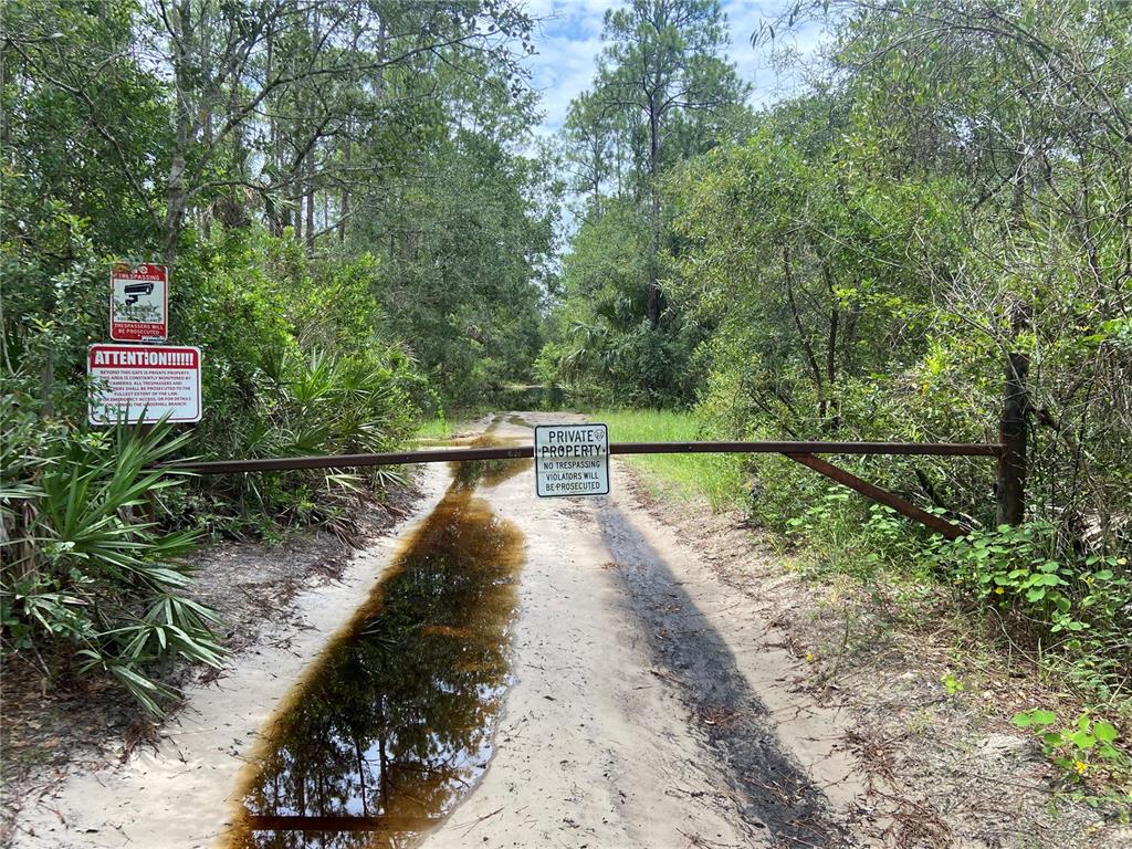 A dirt road is blocked by a metal gate with private property signs in a forest — LAKE HARNEY ROAD, OSTEEN, FL