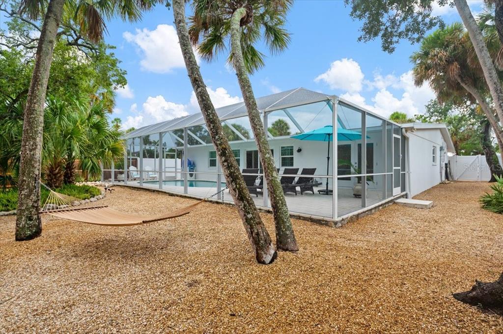 A backyard with a hammock, palm trees, and a screened-in pool enclosure with patio furniture — 5125 SANDY BEACH AVENUE, SARASOTA, FL
