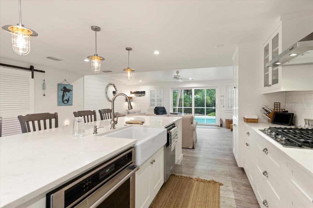 A white kitchen features a farmhouse sink, marble countertops, and a view of a pool — 5125 SANDY BEACH AVENUE, SARASOTA, FL