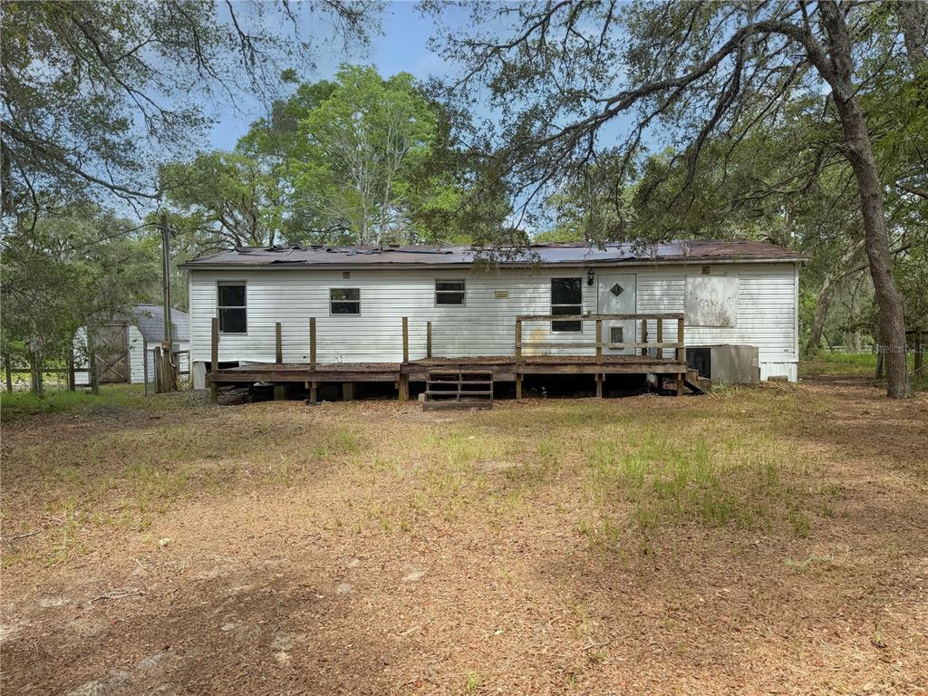 A single-story mobile home with a wooden deck and damaged roof sits in a wooded yard — 8598 N APPENINES POINT, DUNNELLON, FL