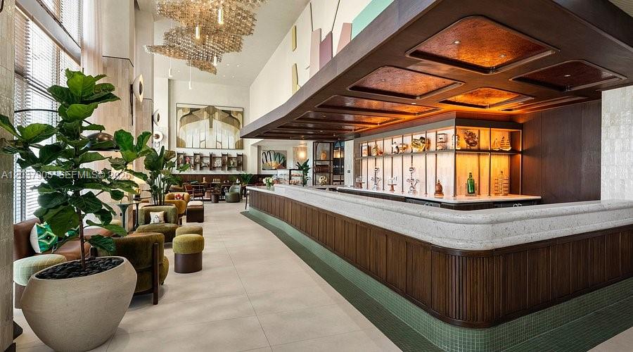 A modern hotel bar features a long stone counter, wood paneling, and a large chandelier — 1611 SW 2nd Ave # 1005, Miami FL 33129, MIAMI, FL
