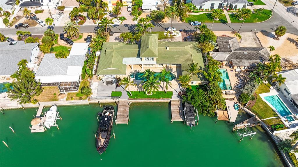 An aerial view shows a waterfront house with a green roof, pool, and boat docks — 482 HERMOSITA DRIVE, ST PETE BEACH, FL
