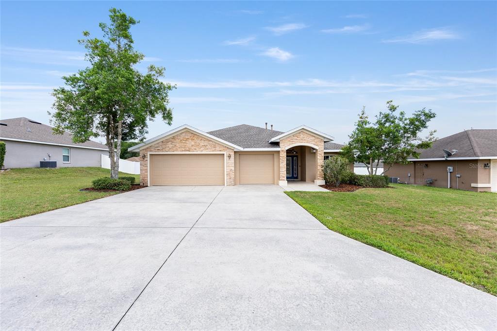 A single-story house with a stone facade, a three-car garage, and a concrete driveway — 915 SE 69TH AVENUE, OCALA, FL