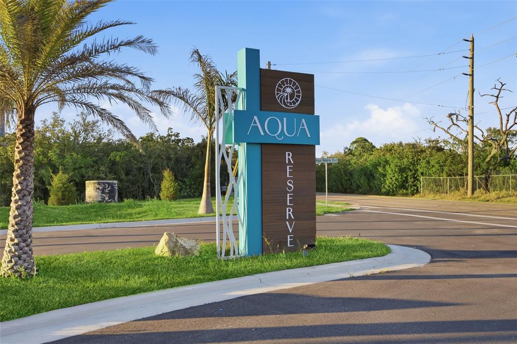 A modern community entrance sign stands on a grassy corner near a paved road — 5968 AQUA RESERVE BOULEVARD, NEW PORT RICHEY, FL