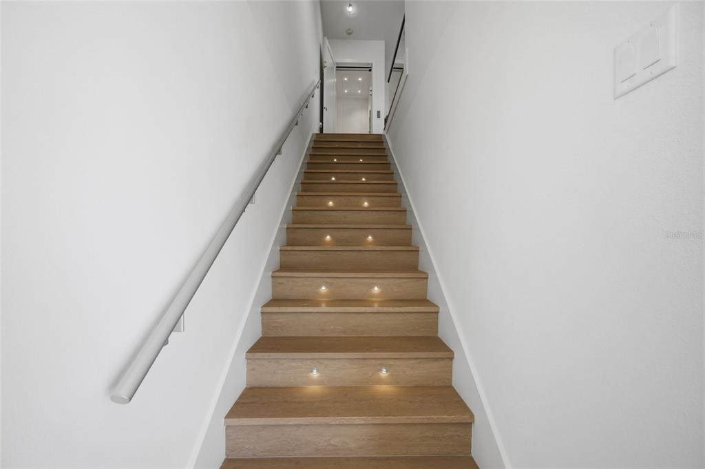 A staircase with light wood steps and integrated recessed lighting leads to a landing — 5968 AQUA RESERVE BOULEVARD, NEW PORT RICHEY, FL