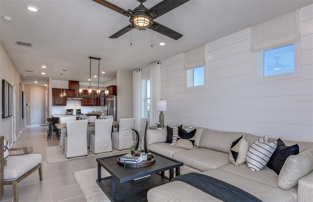 An open-concept living and dining area features a sectional sofa, shiplap wall, and kitchen — 14761 SUNLIT CIRCLE, PARRISH, FL