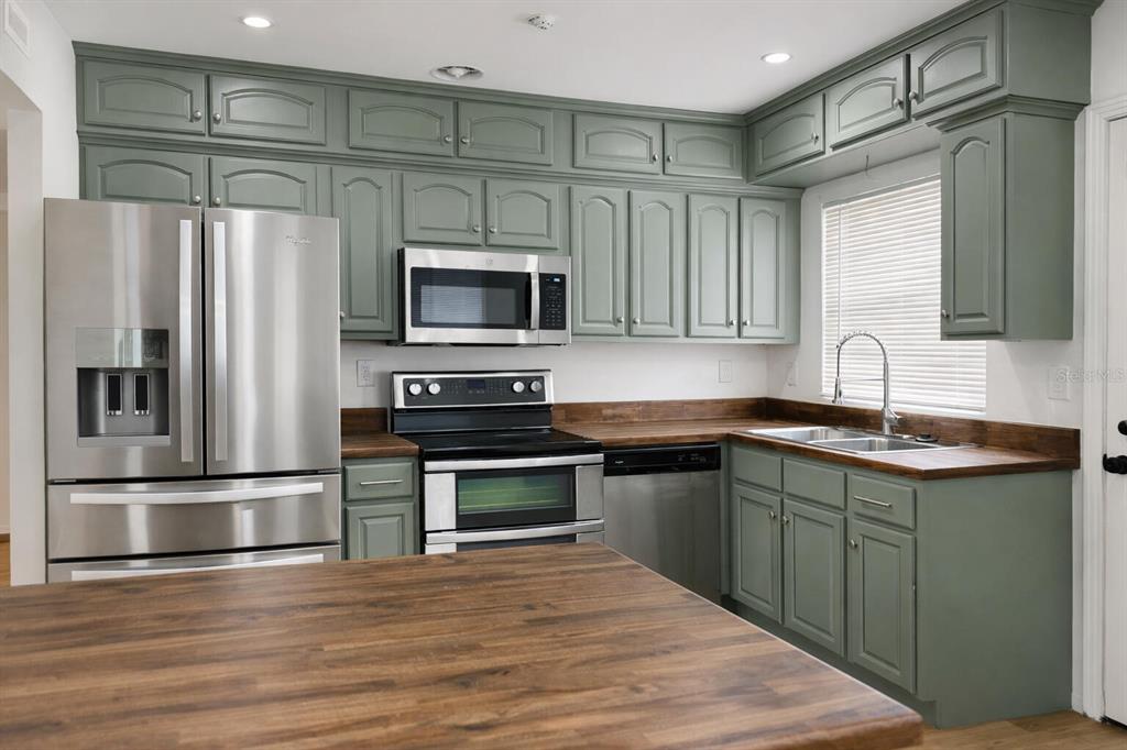 A kitchen features sage green cabinets, stainless steel appliances, and dark wood countertops — 630 TAM O SHANTER DRIVE, ORLANDO, FL