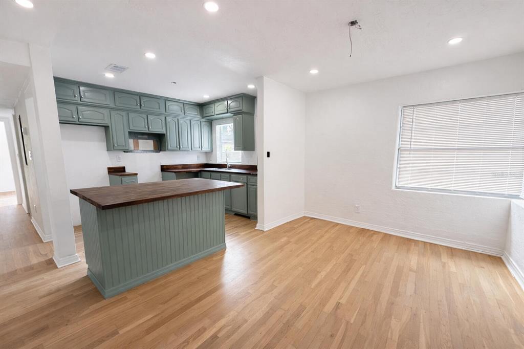 A kitchen with sage green cabinets and a wood countertop island opens to a dining area — 630 TAM O SHANTER DRIVE, ORLANDO, FL