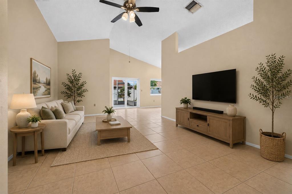 A living room with beige tile floors, a vaulted ceiling, a sofa, and a television console — 5910 BUTTON QUAIL COURT, TAMPA, FL