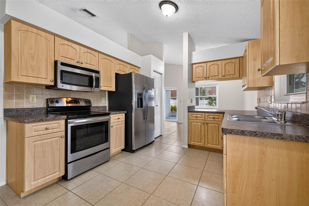 A kitchen features light wood cabinets, stainless steel appliances, dark countertops, and beige tile flooring — 5910 BUTTON QUAIL COURT, TAMPA, FL