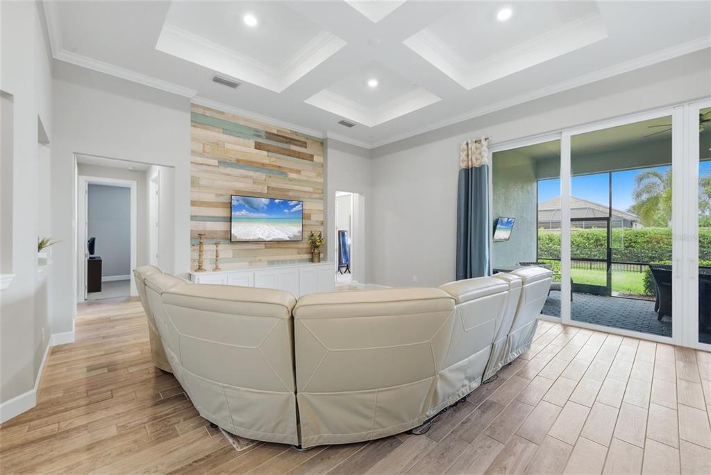 A living room features a wood-paneled accent wall, a curved sofa, and sliding glass doors — 12311 BLUE HILL TRAIL, BRADENTON, FL
