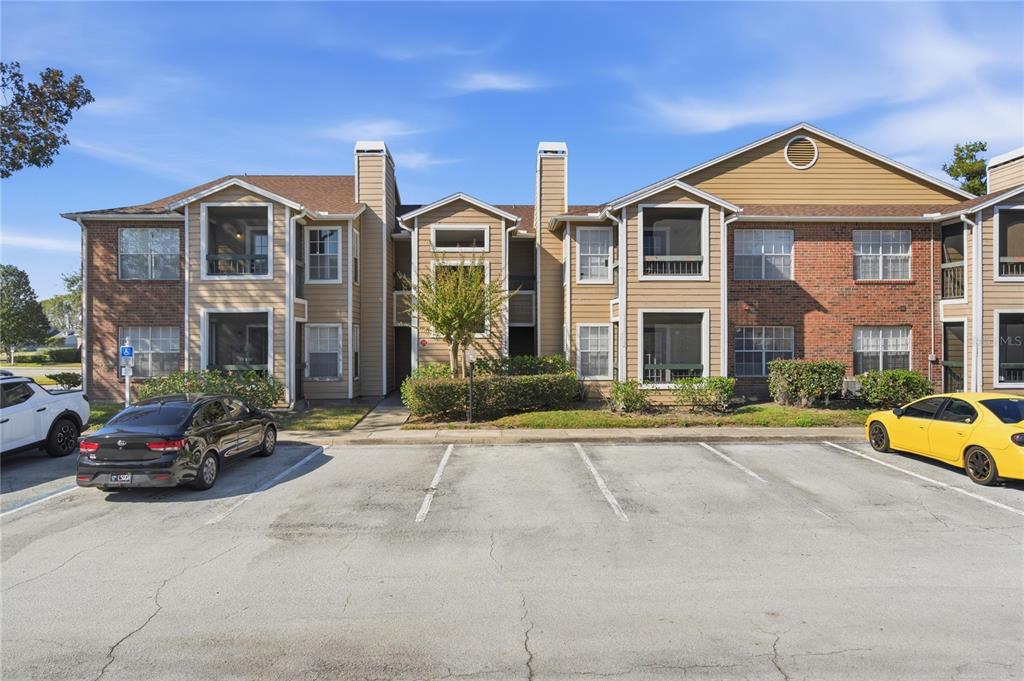 A two-story apartment building with brick and siding exterior, screened balconies, and a parking lot — 4401 THORNBRIAR LANE UNIT R106, ORLANDO, FL