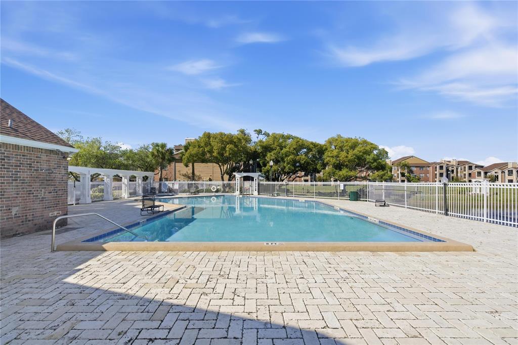 An outdoor swimming pool with a brick deck and white fencing under a blue sky — 4401 THORNBRIAR LANE UNIT R106, ORLANDO, FL