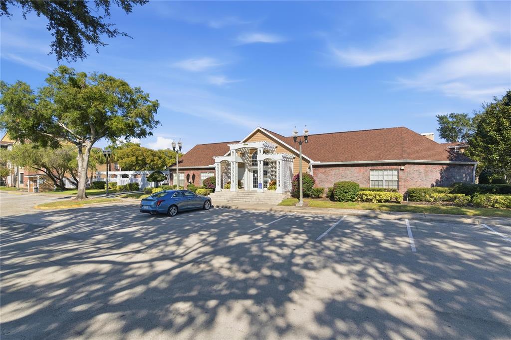 A brick building with a white pergola entrance stands behind a paved parking lot — 4401 THORNBRIAR LANE UNIT R106, ORLANDO, FL