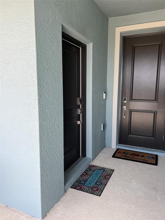 Two dark doors with smart locks are set into a light blue stucco exterior wall — 6488 NEEDLE WAY, ST CLOUD, FL