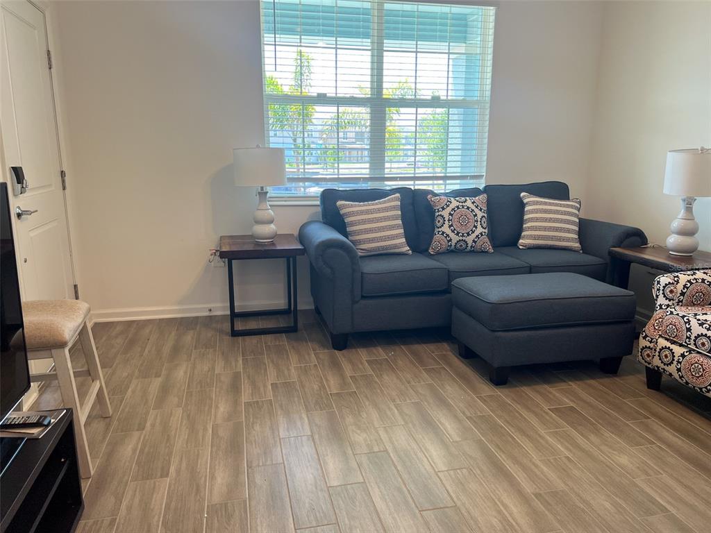 A living room features a blue sofa, matching ottoman, side tables, and wood-look tile flooring — 6488 NEEDLE WAY, ST CLOUD, FL