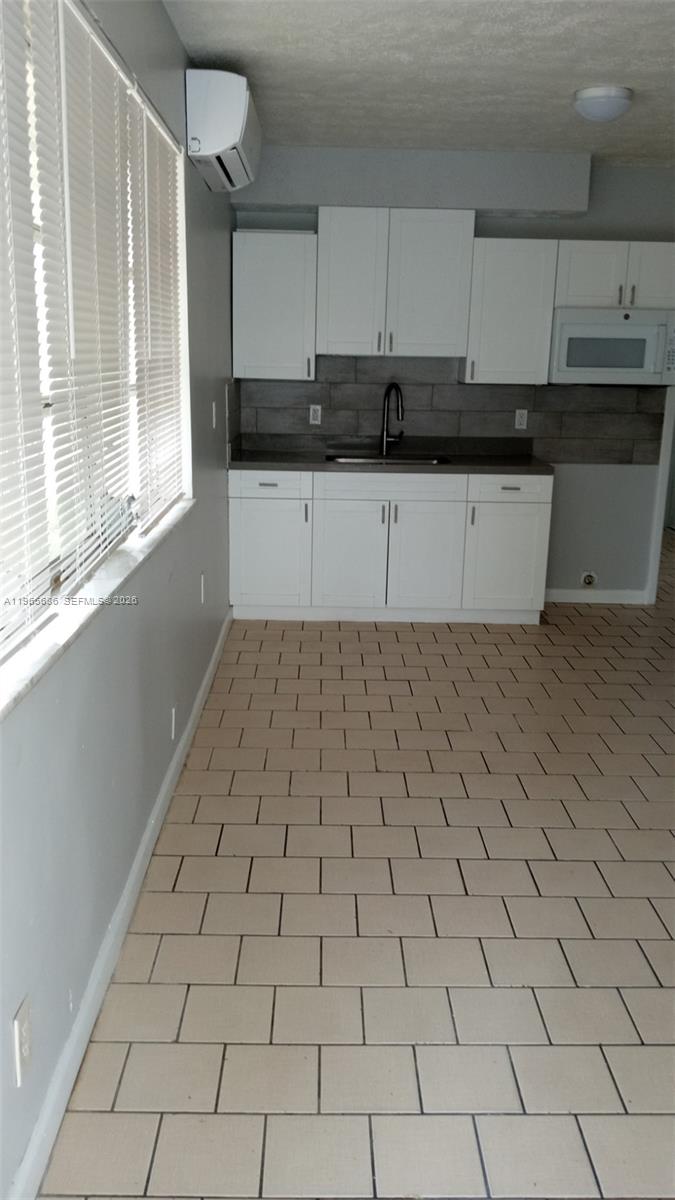 A kitchen features white cabinets, a dark countertop, a tile backsplash, and light-colored floor tiles — 1855 Cleveland St # A, Hollywood FL 33020, HOLLYWOOD, FL