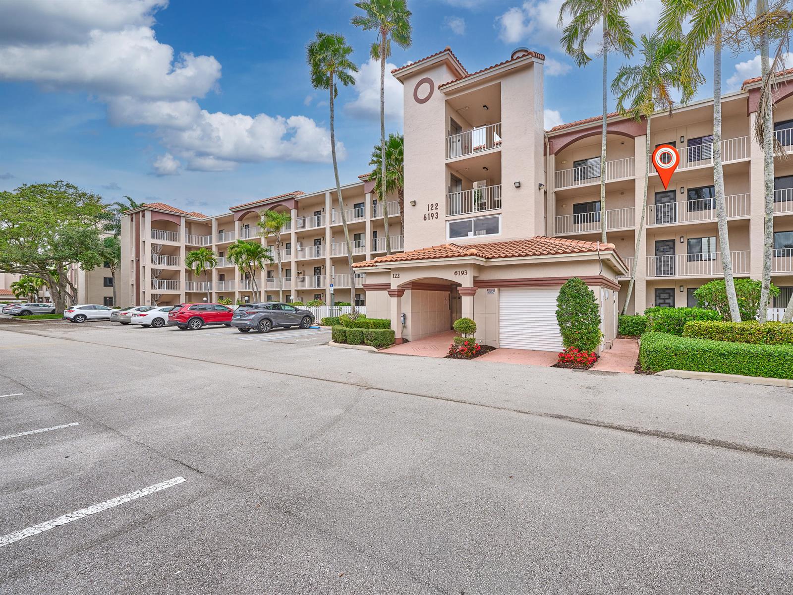 Exterior view of a multi-story apartment building with a parking lot and palm trees — 6193 Pointe Regal Circle # 306, Delray Beach FL 33484, DELRAY BEACH, FL