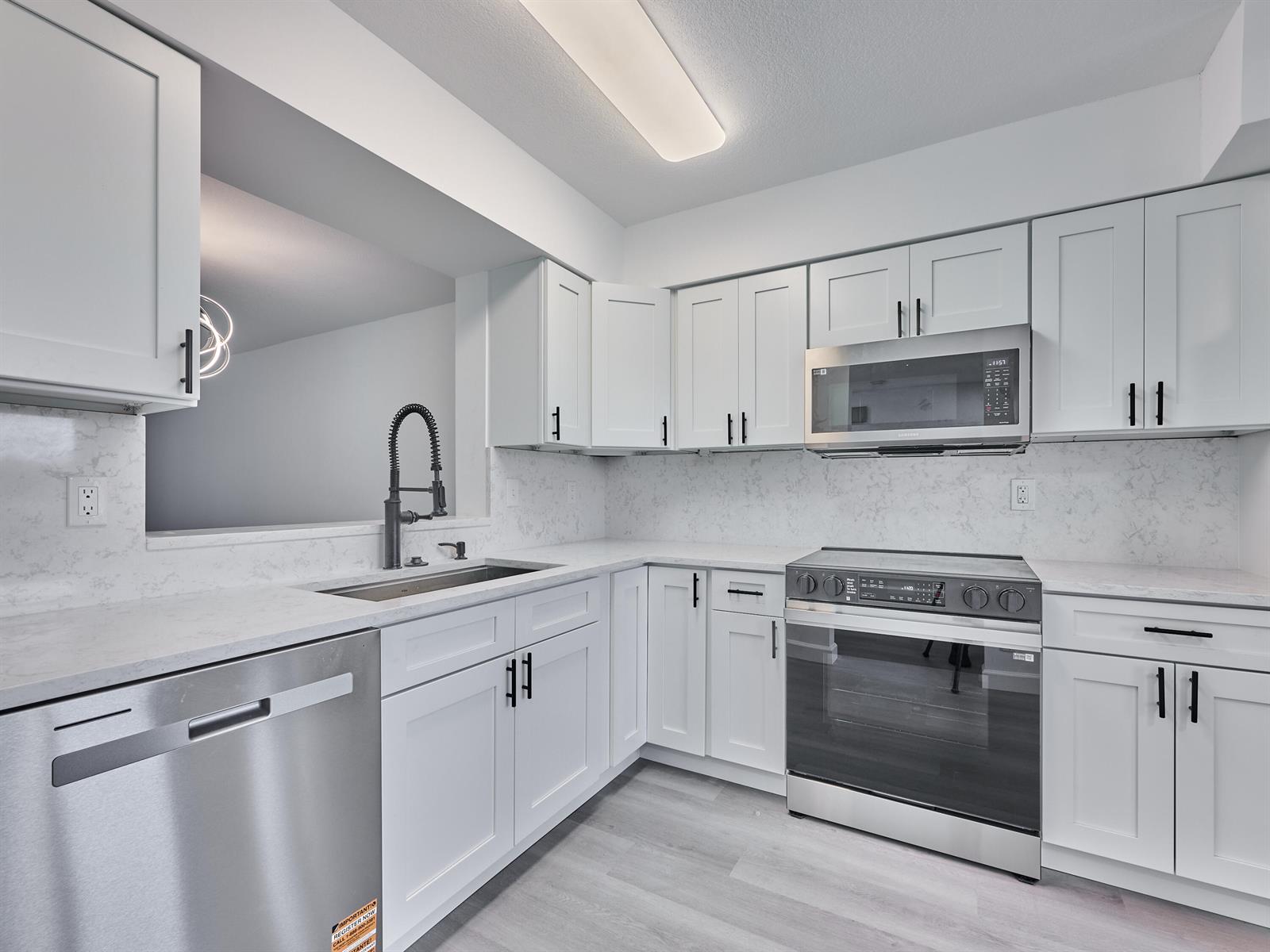 A modern kitchen features white cabinets, stainless steel appliances, and light-colored quartz countertops — 6193 Pointe Regal Circle # 306, Delray Beach FL 33484, DELRAY BEACH, FL