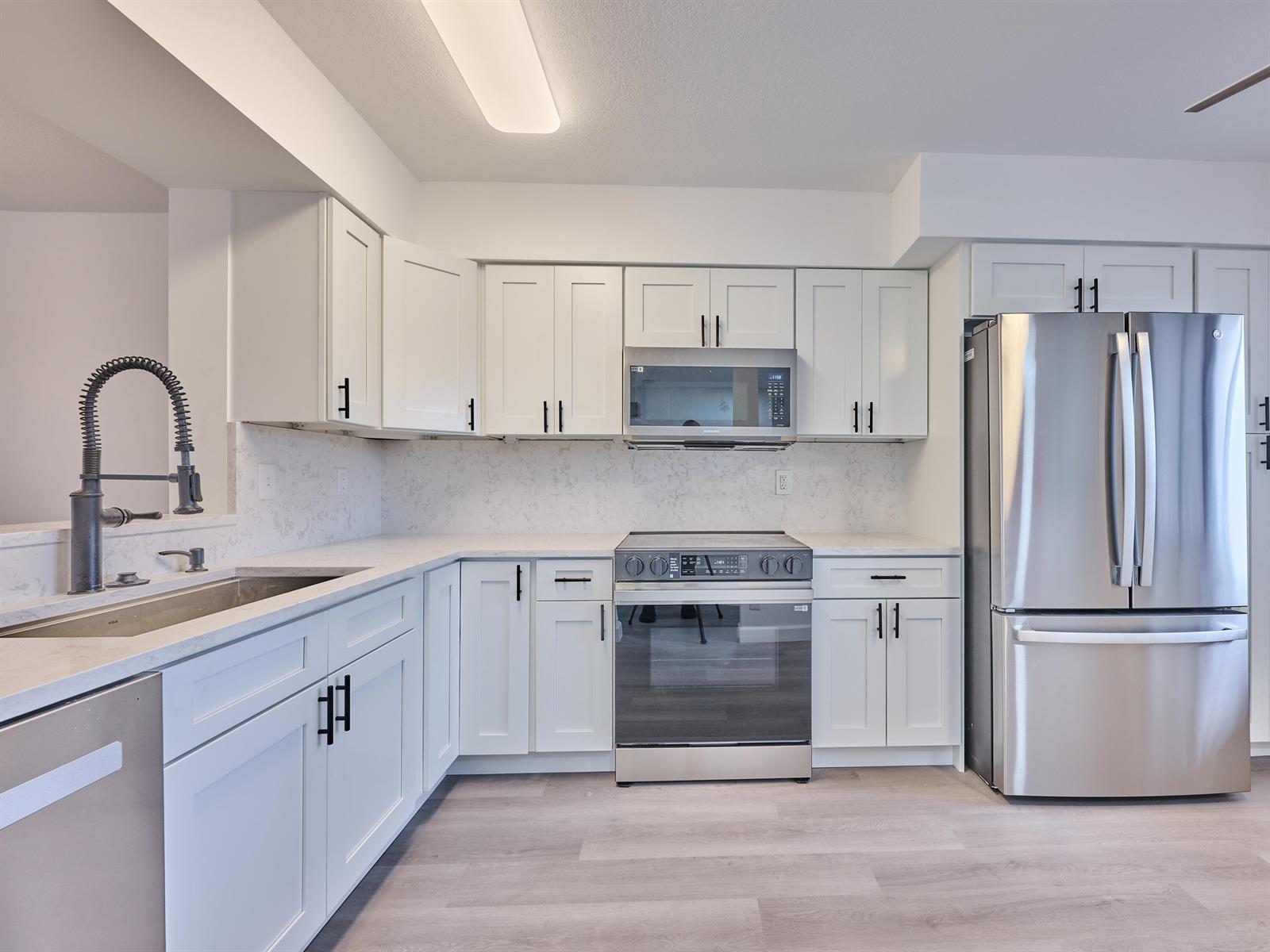 A modern kitchen features white cabinets, stainless steel appliances, and light-colored quartz countertops — 6193 Pointe Regal Circle # 306, Delray Beach FL 33484, DELRAY BEACH, FL
