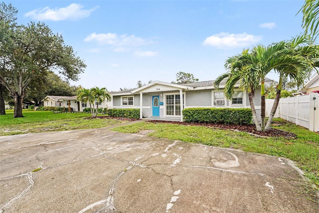 A single-story house with a blue front door, a cracked concrete driveway, and palm trees — 766 41ST AVENUE NE, ST PETERSBURG, FL