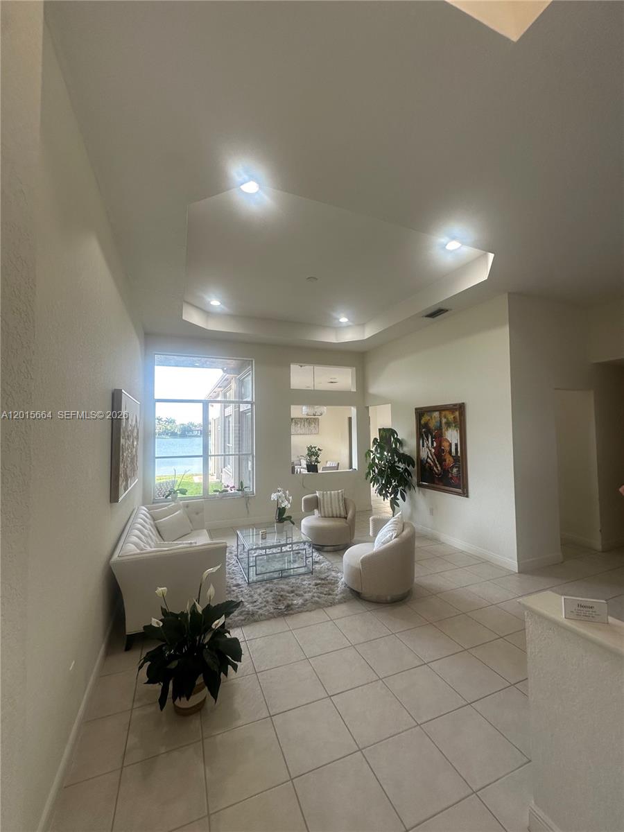 A bright living room features a tray ceiling, tile flooring, and a large window view — 18571 SW 44th St, Miramar FL 33029, MIRAMAR, FL