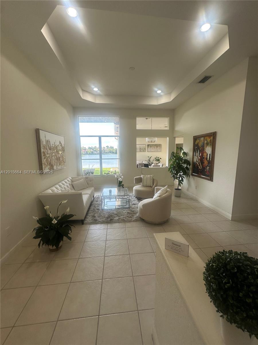 A bright living room features a high tray ceiling, tile flooring, and a lake view — 18571 SW 44th St, Miramar FL 33029, MIRAMAR, FL