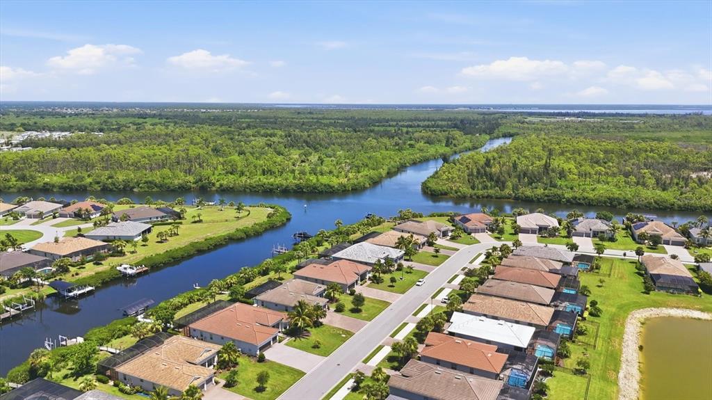 An aerial view shows a suburban neighborhood with houses bordering a canal and wooded area — 15040 SPANISH POINT DRIVE, PORT CHARLOTTE, FL
