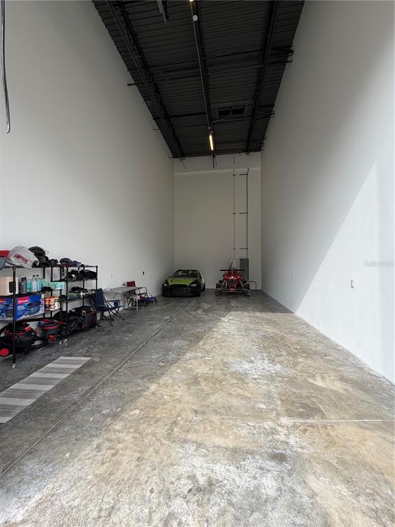 A high-ceilinged garage with concrete floors, white walls, storage shelving, and two parked vehicles — 6500 MOTOR ENCLAVE WAY UNIT 1216, TAMPA, FL
