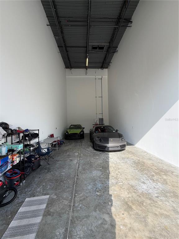 A high-ceilinged garage with concrete floors houses two parked cars and storage shelving — 6500 MOTOR ENCLAVE WAY UNIT 1216, TAMPA, FL