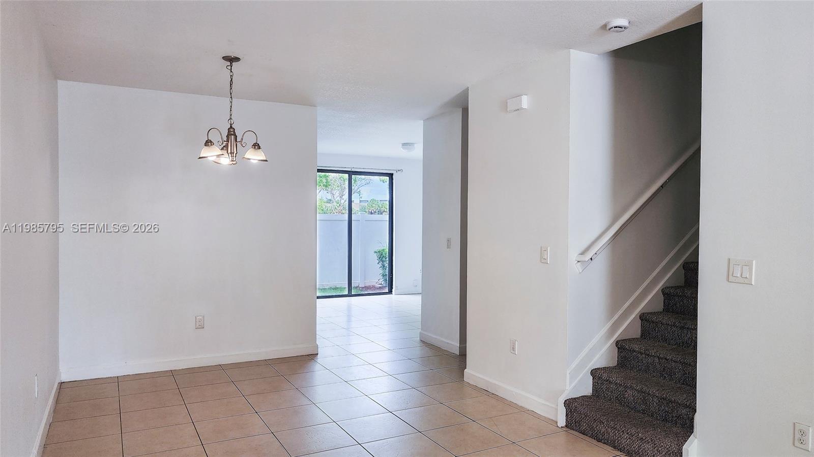 An interior view shows a tiled dining area with a chandelier and carpeted stairs — 470 NE 194th Ter # 470, Miami FL 33179, MIAMI, FL