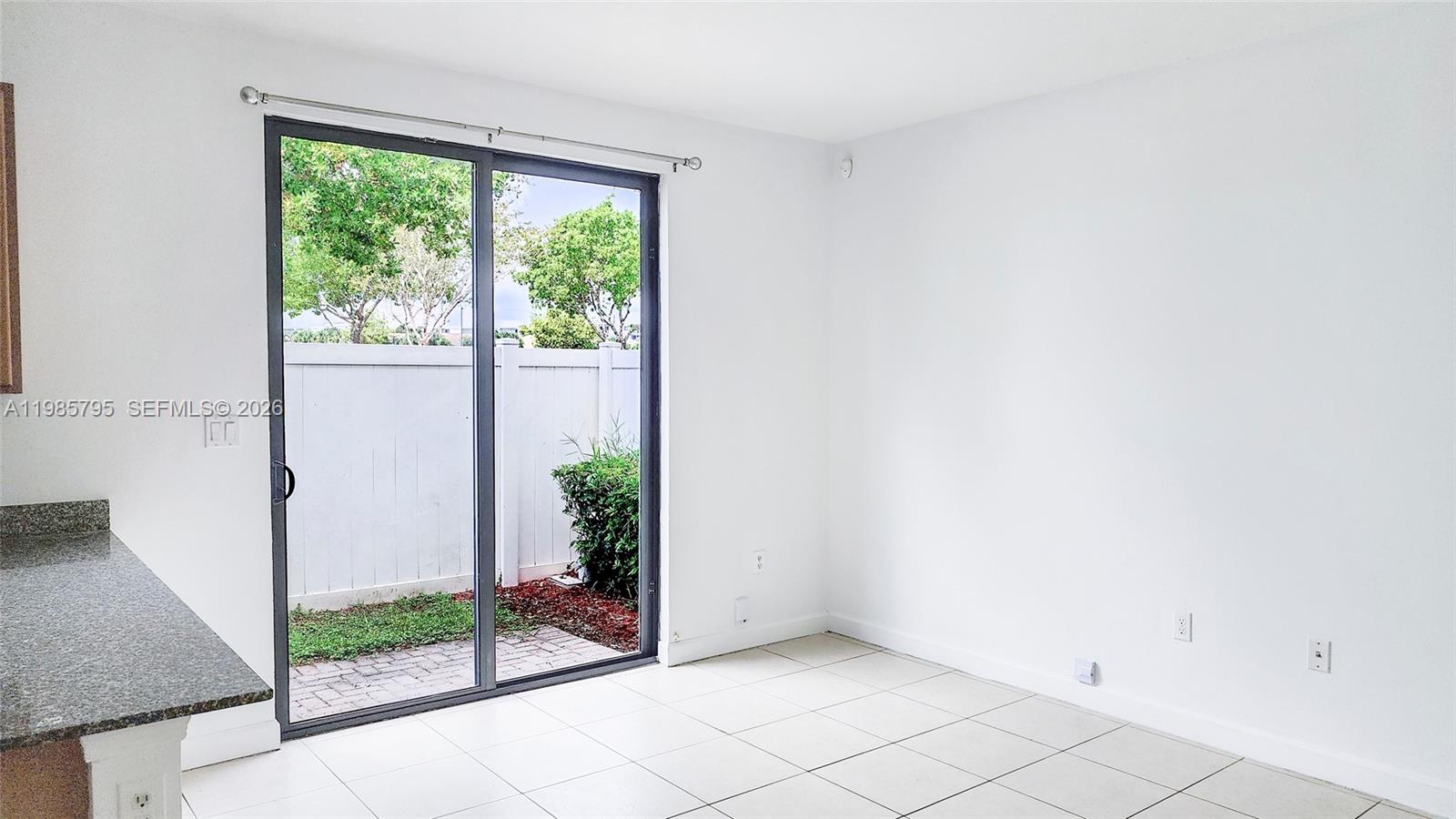 An empty room with white walls, tiled floors, and a sliding glass door to a patio — 470 NE 194th Ter # 470, Miami FL 33179, MIAMI, FL