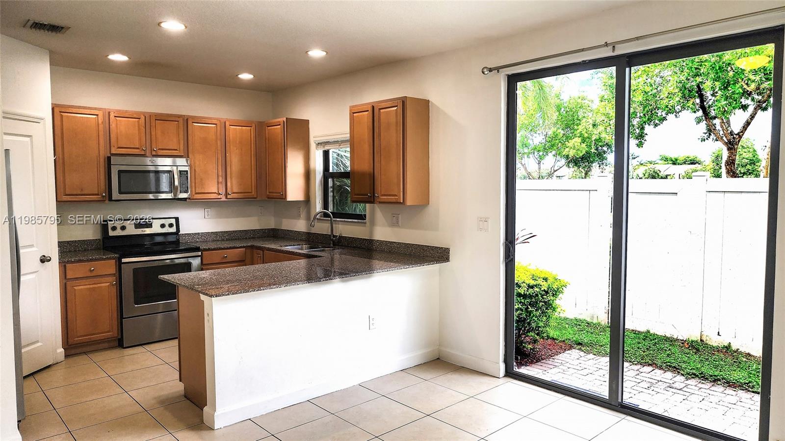 A kitchen features wooden cabinets, granite countertops, stainless steel appliances, and a sliding glass door — 470 NE 194th Ter # 470, Miami FL 33179, MIAMI, FL