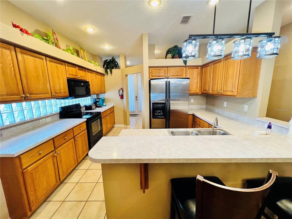 A kitchen with wood cabinets, stainless steel appliances, and a breakfast bar with pendant lighting — 2918 SUNSET VISTA BOULEVARD, KISSIMMEE, FL