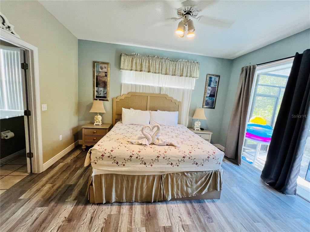 A bedroom features a queen bed with towel swans, light blue walls, and wood-look flooring — 2918 SUNSET VISTA BOULEVARD, KISSIMMEE, FL