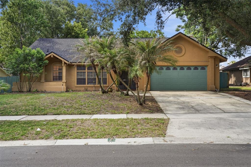 A single-story tan house with a green garage door and palm trees in the front yard — 733 SWAYING PALM DRIVE, APOPKA, FL