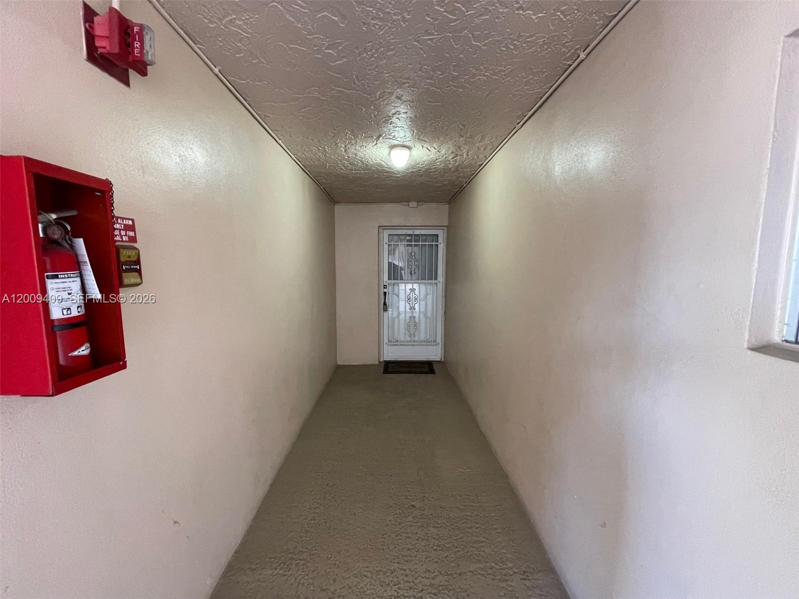 A narrow hallway features a red fire extinguisher cabinet, a fire alarm, and a door — 9471 Evergreen Pl # 401, Davie FL 33324, DAVIE, FL