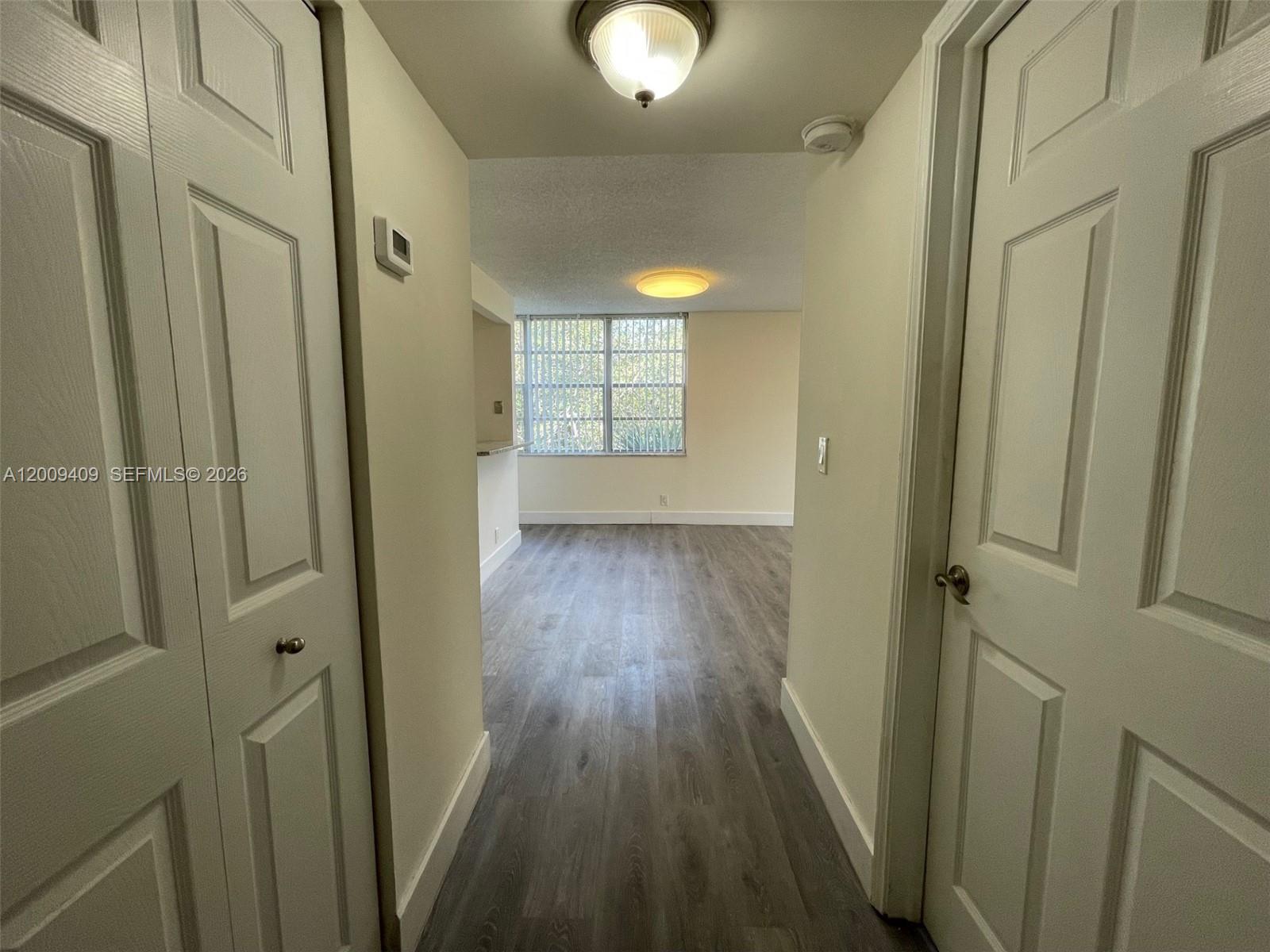 A hallway with light wood-look flooring leads to a living area with a large window — 9471 Evergreen Pl # 401, Davie FL 33324, DAVIE, FL