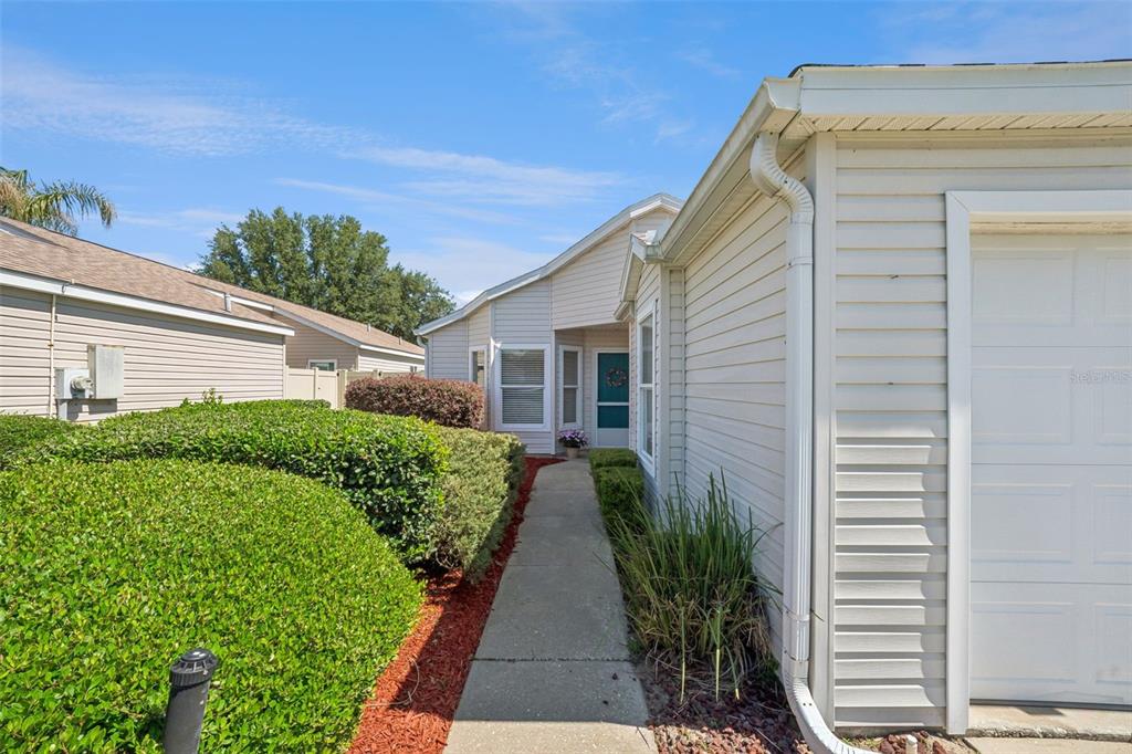 A concrete walkway leads to the front entrance of a house with light-colored siding — 4967 HERON RUN CIRCLE, LEESBURG, FL