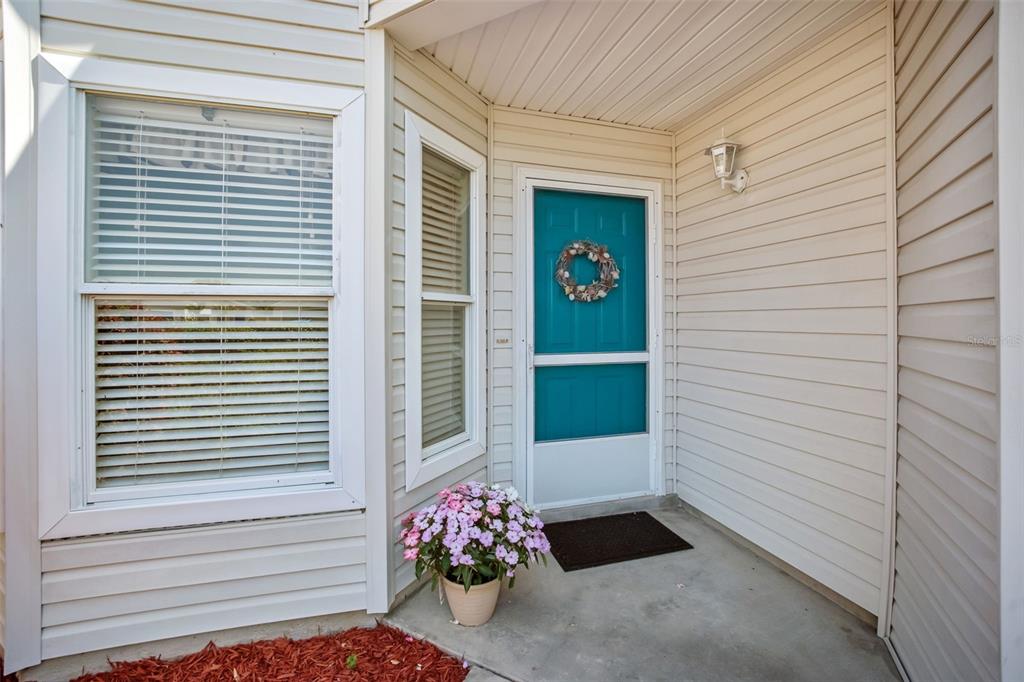 A teal front door with a wreath sits on a porch with light-colored siding — 4967 HERON RUN CIRCLE, LEESBURG, FL