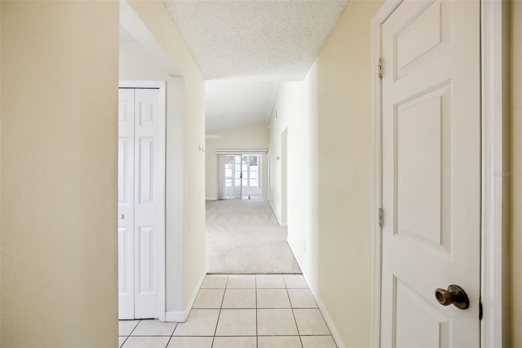 A hallway with tiled flooring leads to a carpeted living area with sliding glass doors — 4967 HERON RUN CIRCLE, LEESBURG, FL