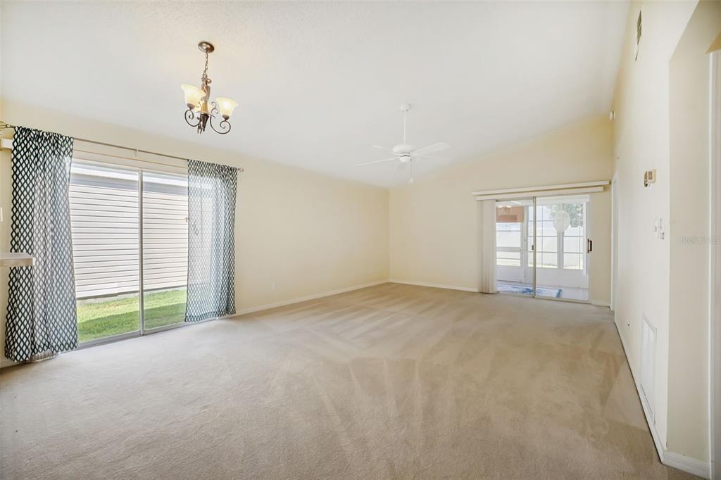 A spacious living room features beige carpeting, a ceiling fan, and two sliding glass doors — 4967 HERON RUN CIRCLE, LEESBURG, FL