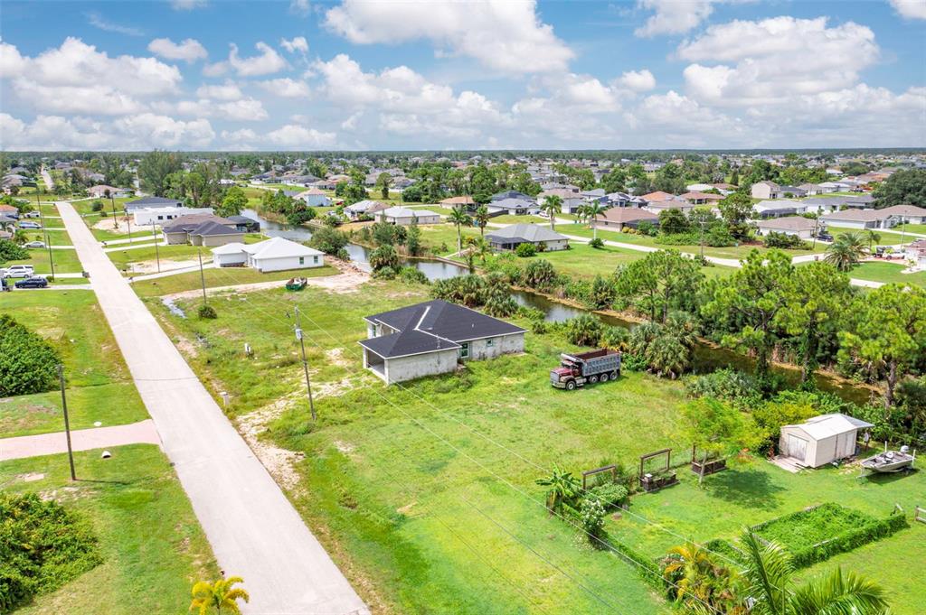 An aerial view shows a house under construction on a grassy lot with a canal — 1623 NE 36TH LANE, CAPE CORAL, FL