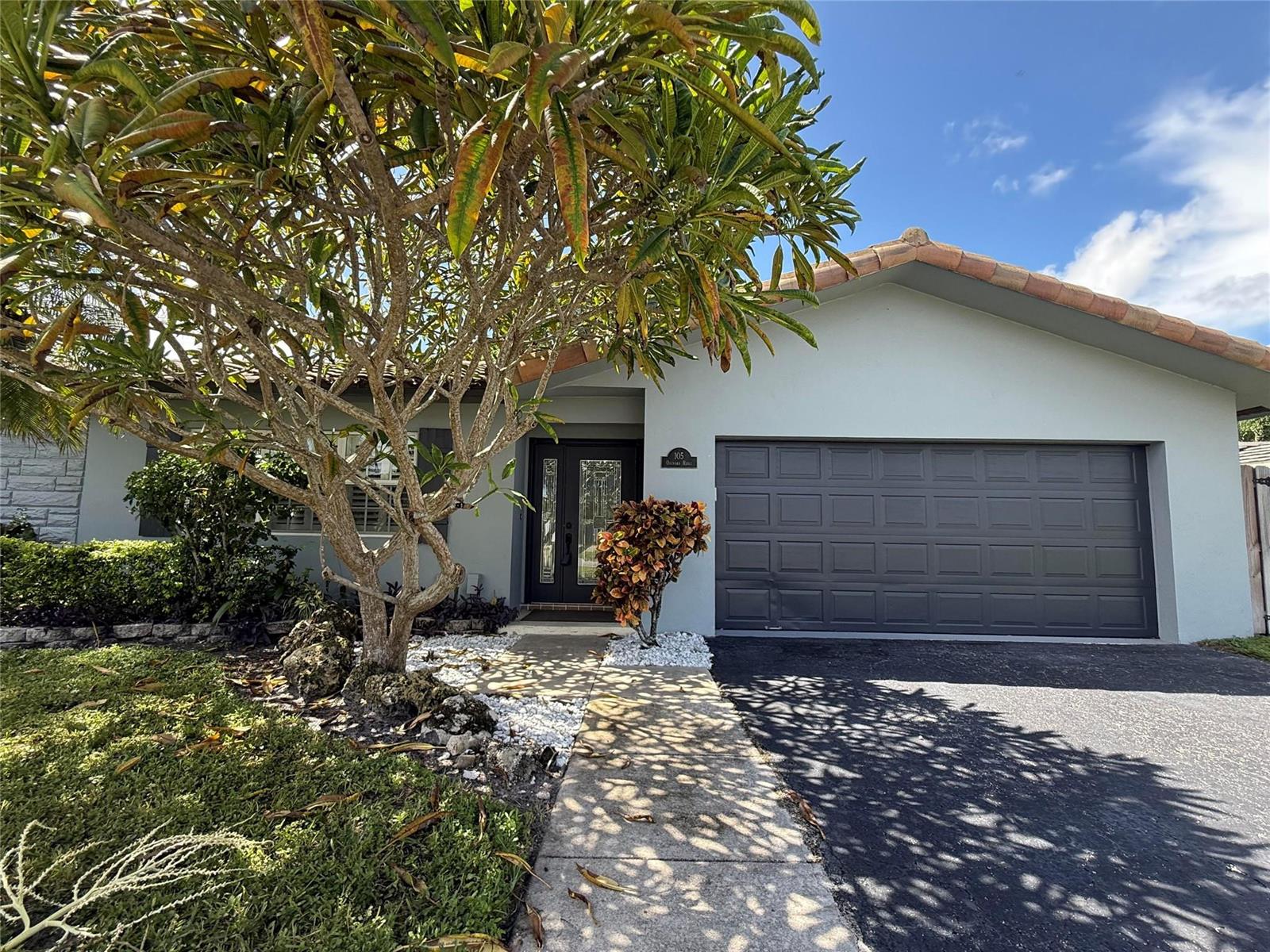 A single-story house features a gray exterior, a dark garage door, and a large tree — 105 Orchard Ridge Lane, Boca Raton FL 33431, BOCA RATON, FL