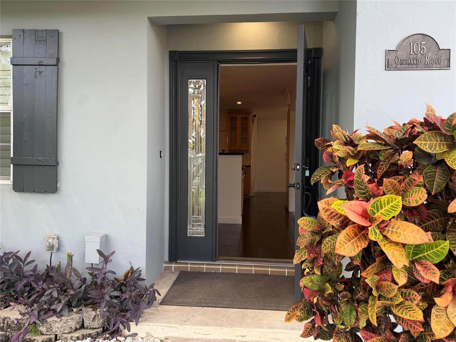 A front entrance with a dark gray door, a decorative glass panel, and colorful croton plants — 105 Orchard Ridge Lane, Boca Raton FL 33431, BOCA RATON, FL