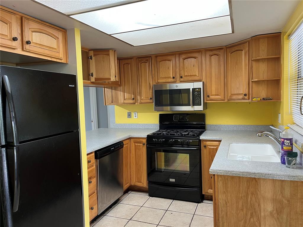 A kitchen features oak cabinets, black appliances, a yellow wall, and gray laminate countertops — 207 BIRCH TERRACE, WINTER SPRINGS, FL